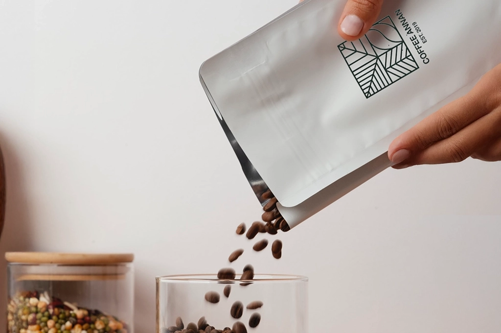 Hochwertige Kaffeebohnen werden aus einer stilvollen, nachhaltigen Verpackung in ein Glas gegossen – Symbol für Qualität, Präzision und nachhaltige PPWR-Lösungen, die Valean Solutions als verlässlicher Partner bietet.